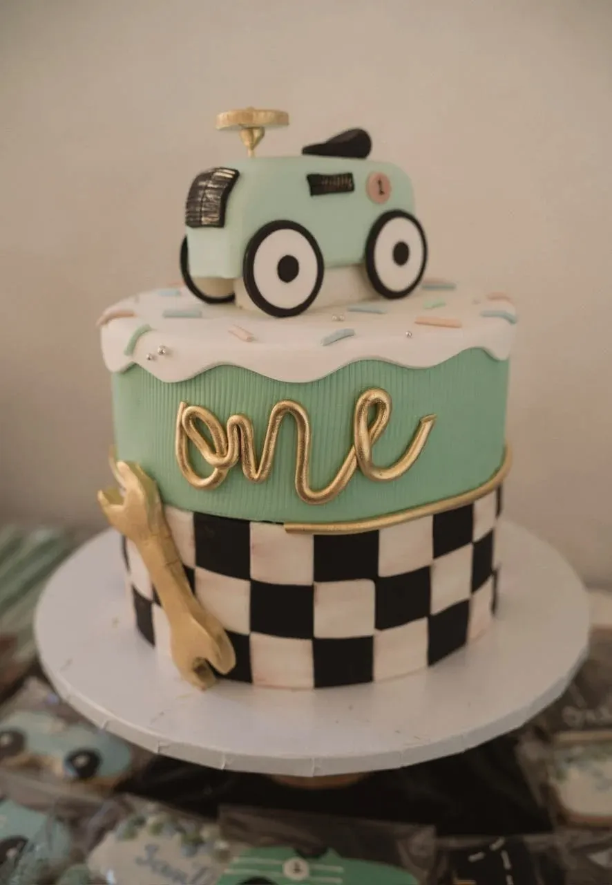 A mint and gold one cake with a checkered flag base, a fondant wrench, and a little race car on top