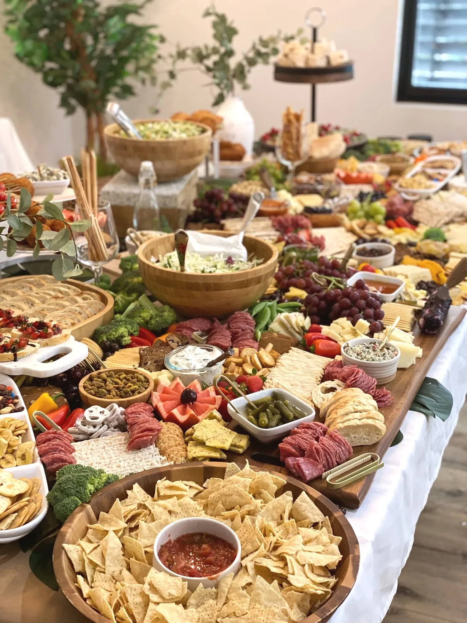 A close view of the grazing table with salami, cheeses, crackers, sliced watermelon, and a bowl of chips and salsa