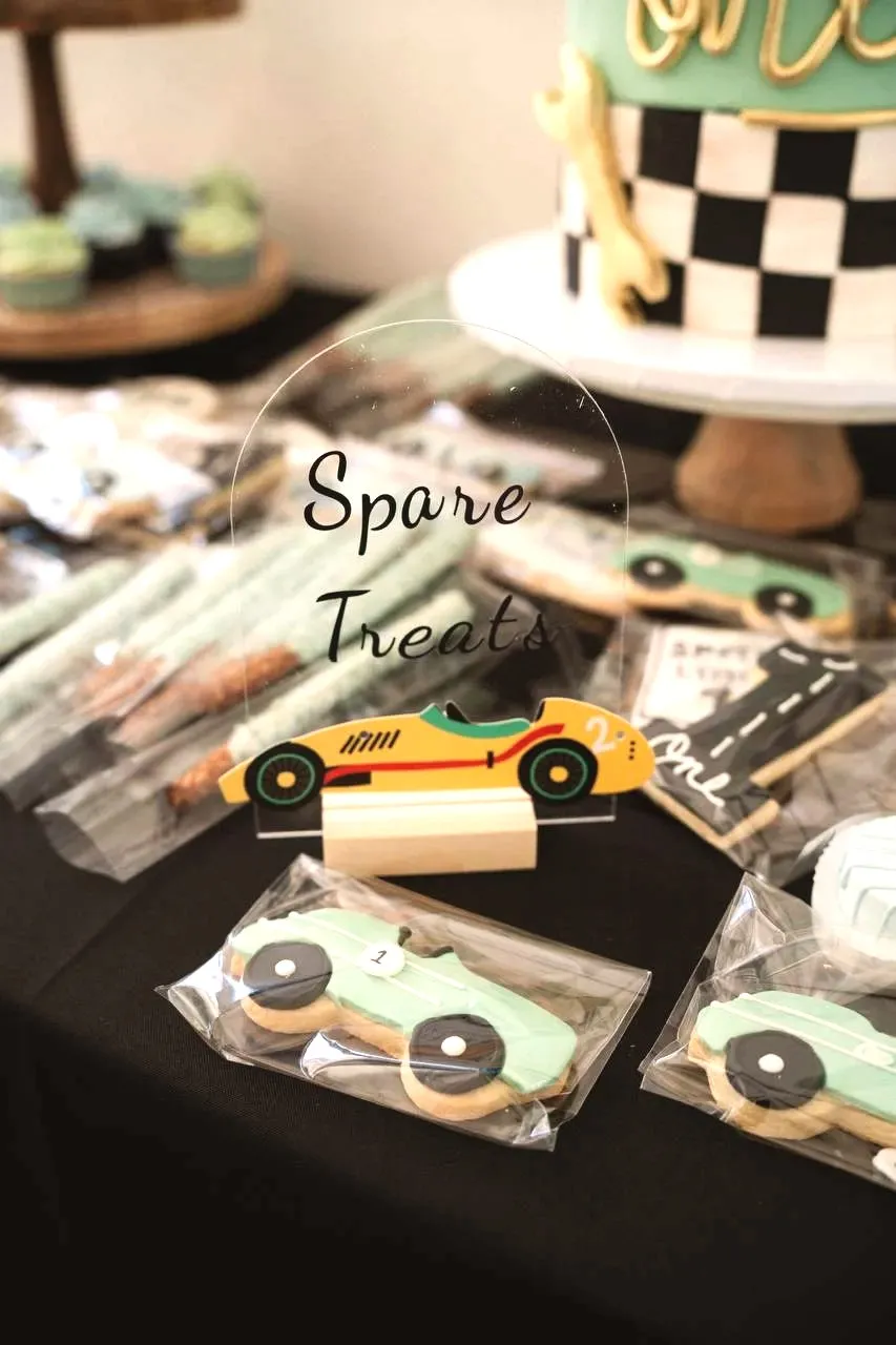 A Spare Treats sign beside iced race car cookies in cellophane bags on a black tablecloth