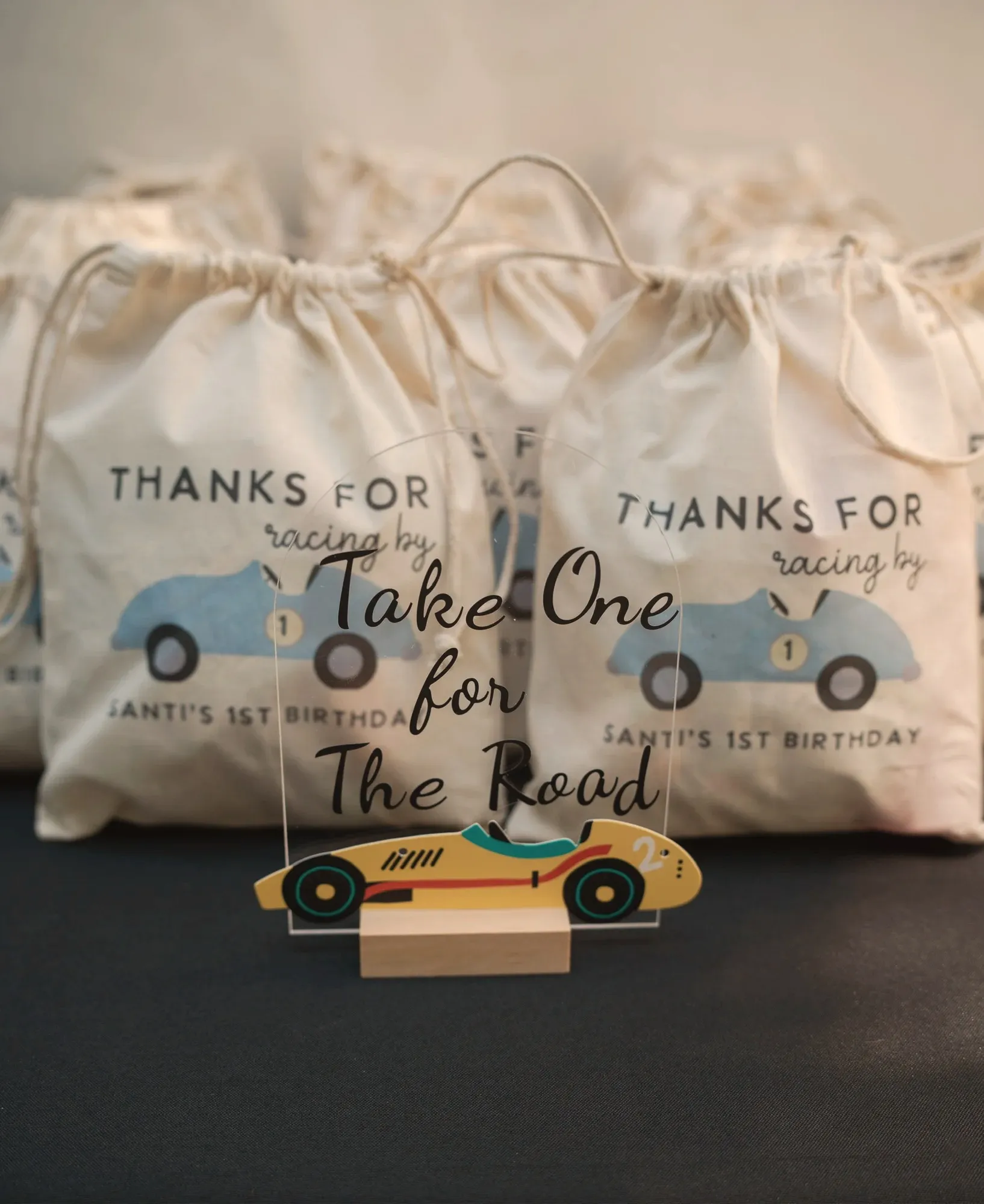 Cotton favor bags reading thanks for racing by, Santi's 1st birthday, beside a Take One for the Road sign