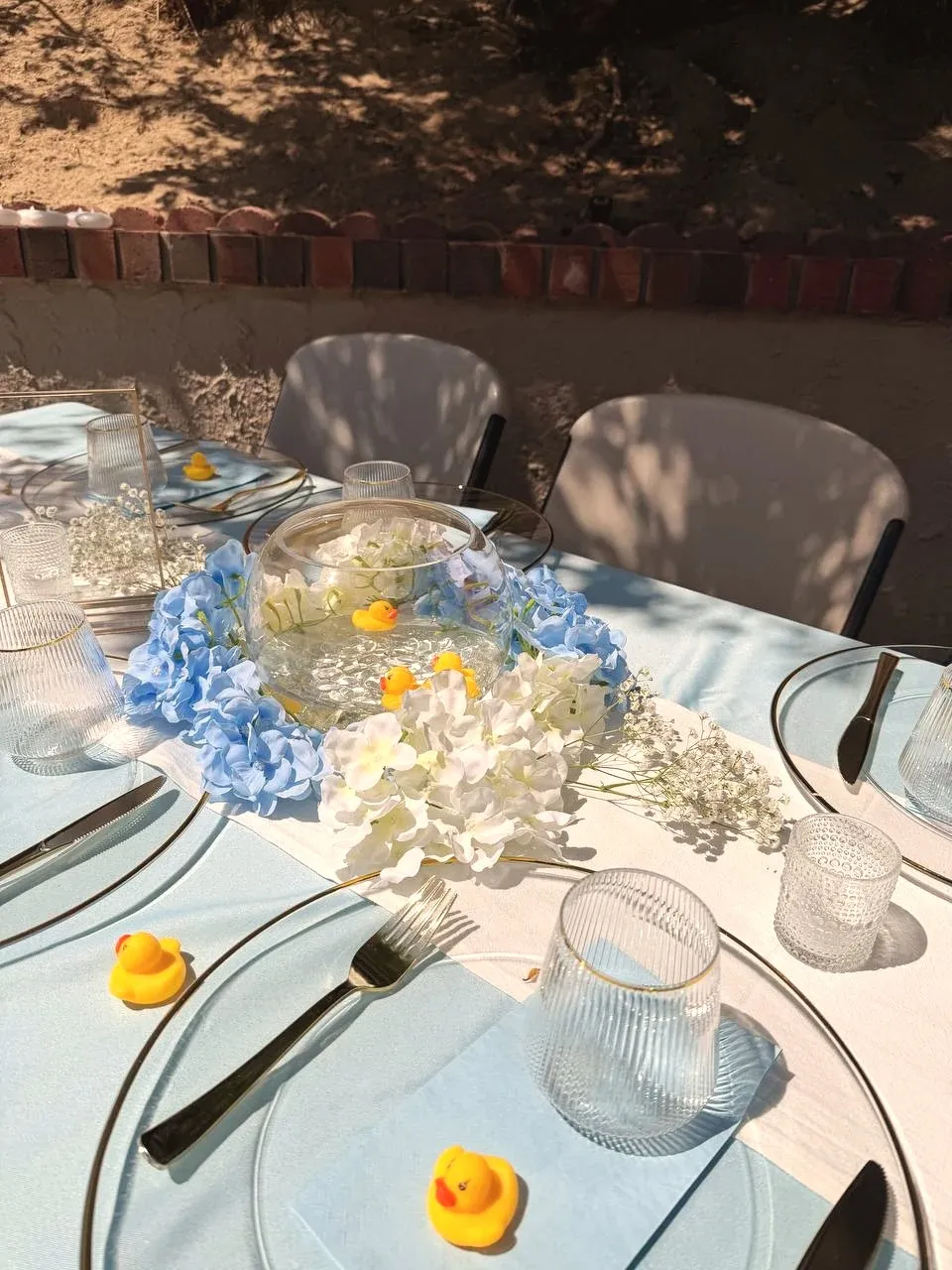 The center of the table in afternoon sun, fishbowl and hydrangea on a white runner.