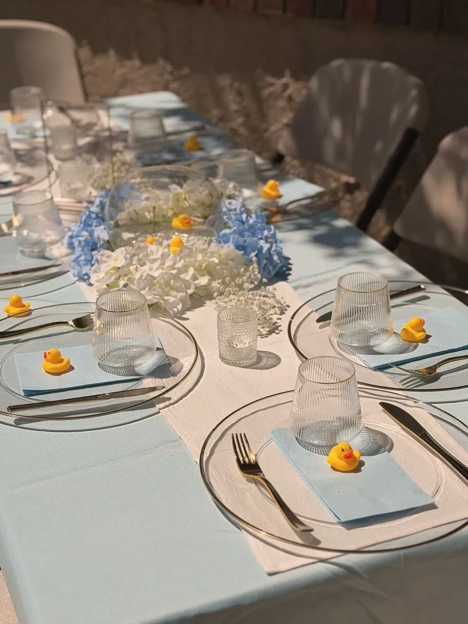 Place settings down one side of the table, gold-rimmed chargers on pale blue linen.
