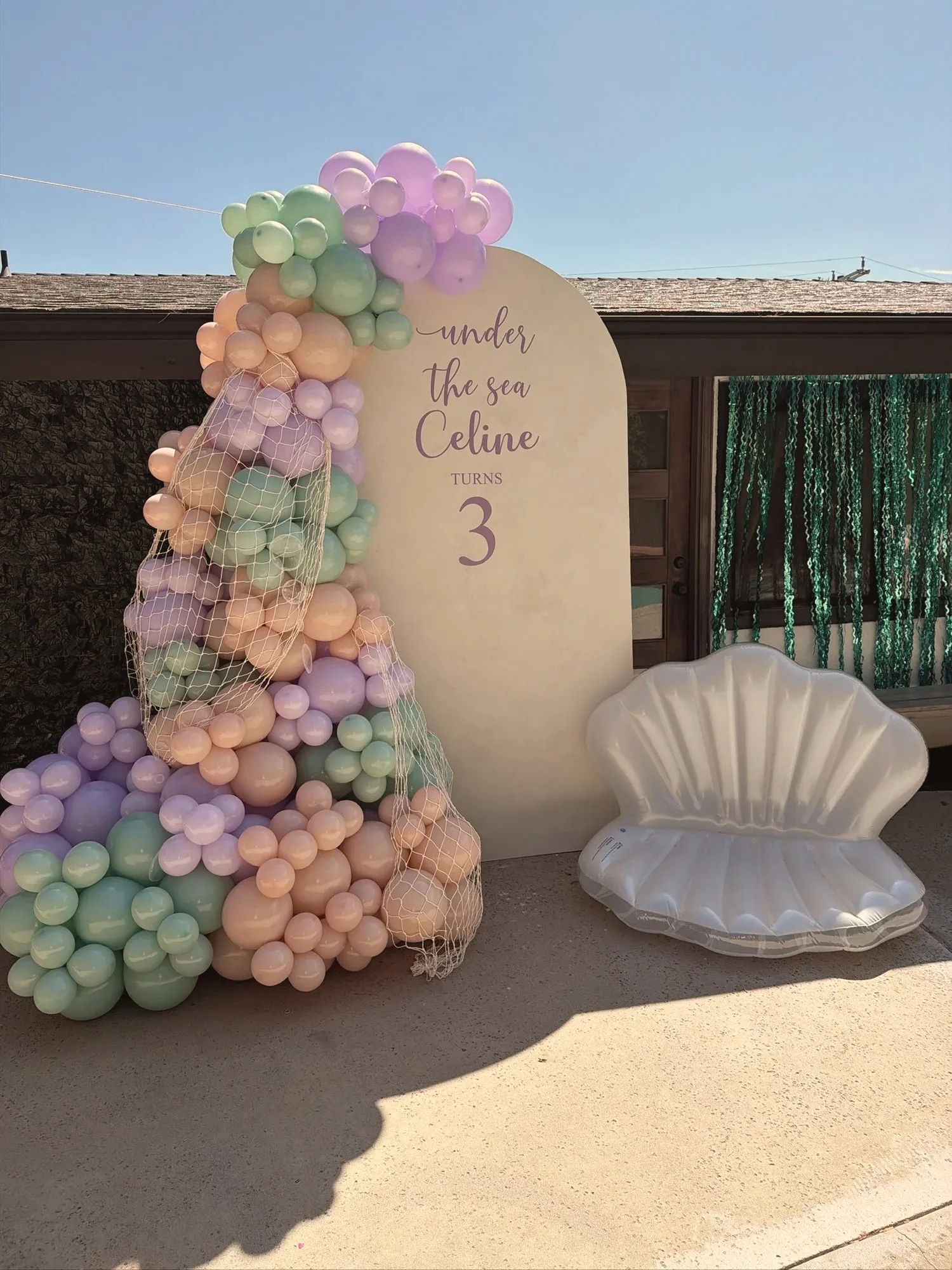 The arched Under The Sea sign in the middle of the day, with an inflatable white clamshell chair beside it and turquoise streamers hanging in the doorway behind